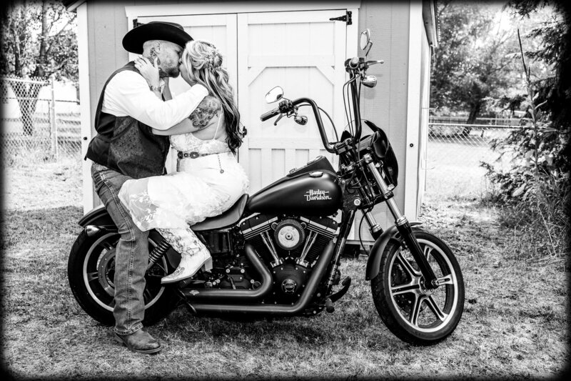 Bride and Groom sitting face to face kissing on the back of a motorcycle.