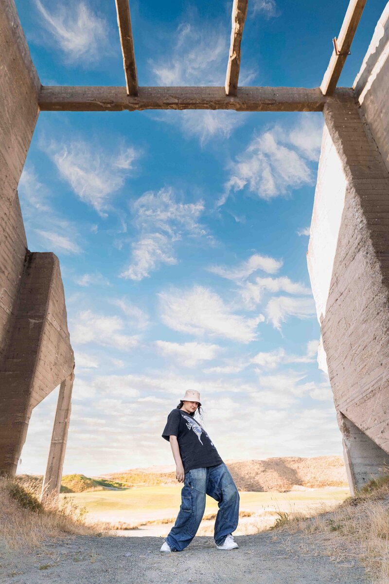 Epic photo of Tacoma senior graduate standing under stone structure  with clouds in blue sky behind her.
