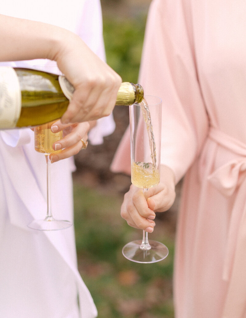 November wedding at Graylyn Estate, designed and planned by Charming Carolina — bride and bridesmaids popping champagne while getting ready with hair and makeup artists in the bridal suite.