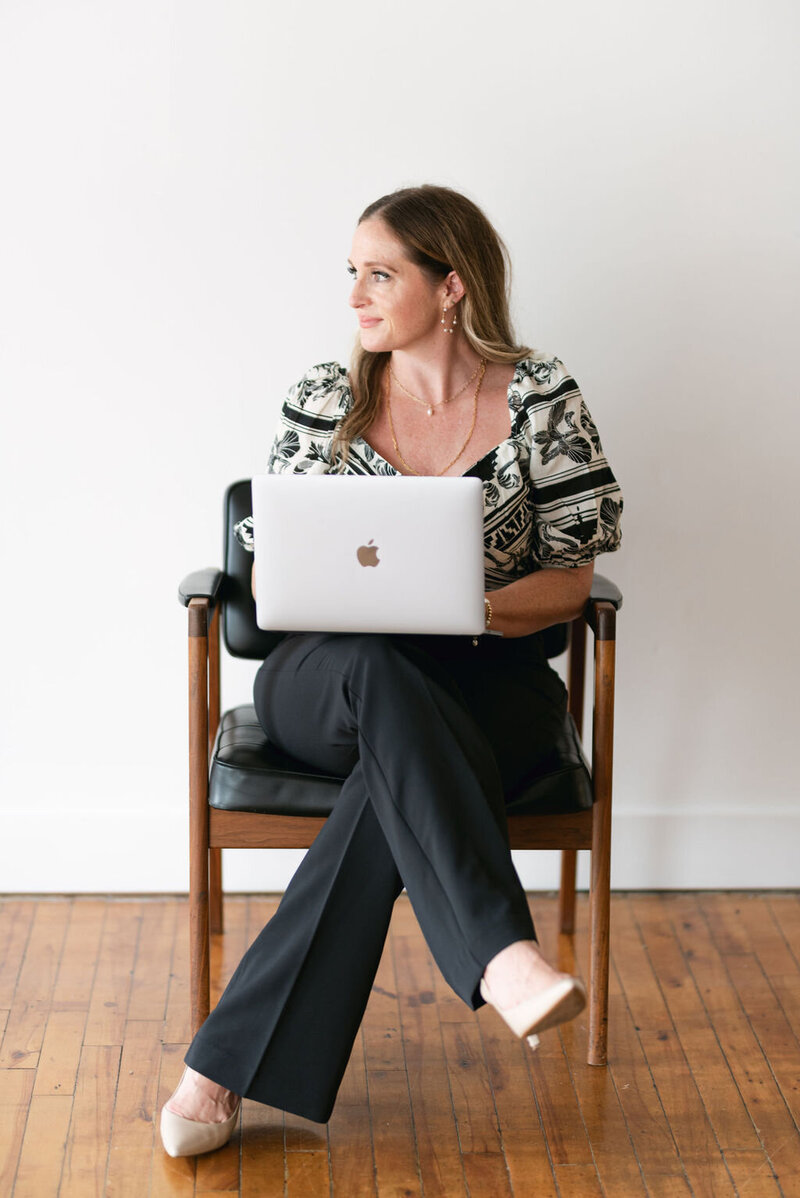 A woman sitting in a chair with a laptop looking away from the camera