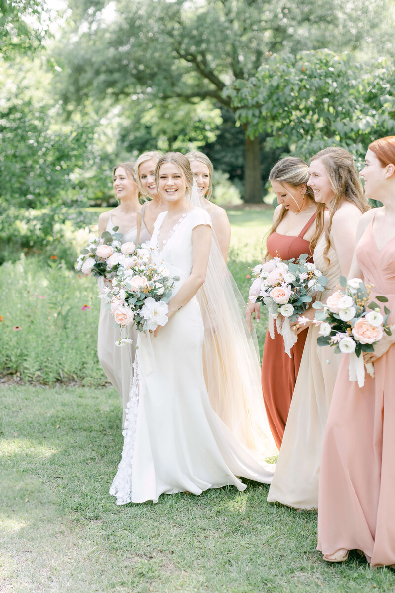 A bride smiles while walking in front of her bridesmaids.