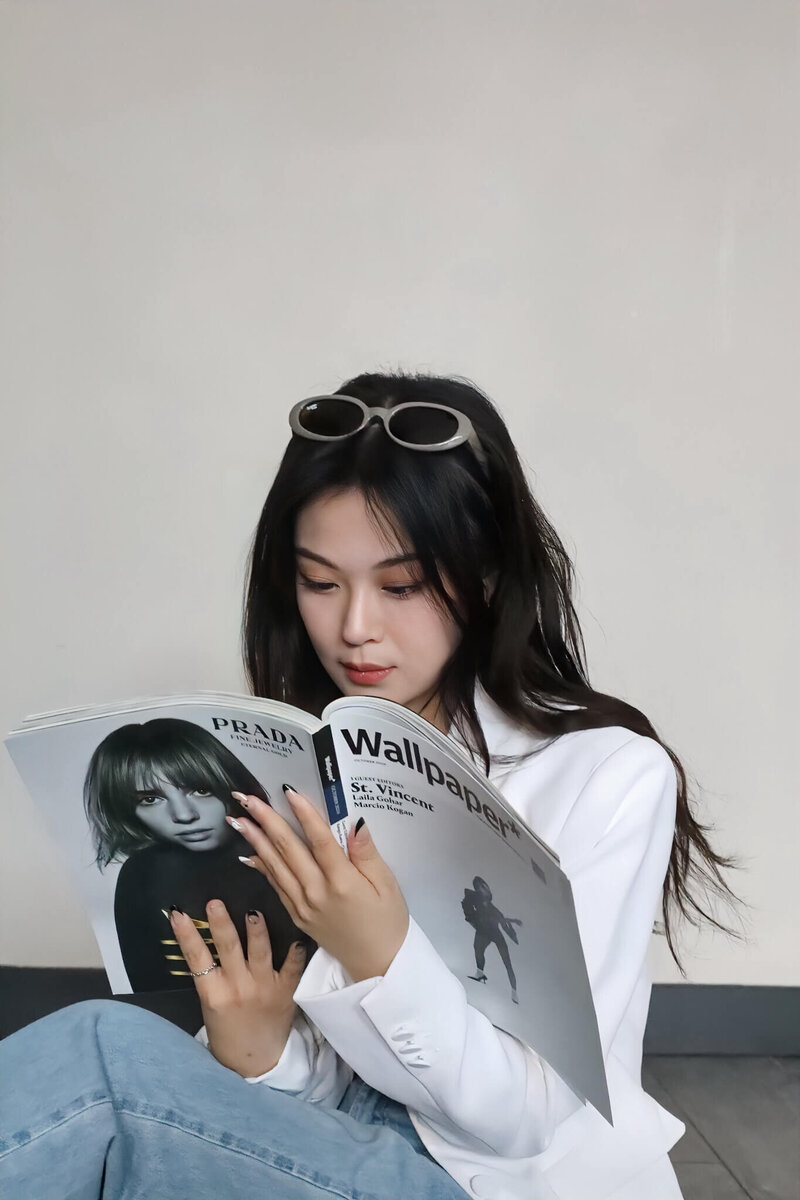 Web designer Jenny in a white blazer and sunglasses on her head, reading Wallpaper magazine, capturing a chic and modern look.