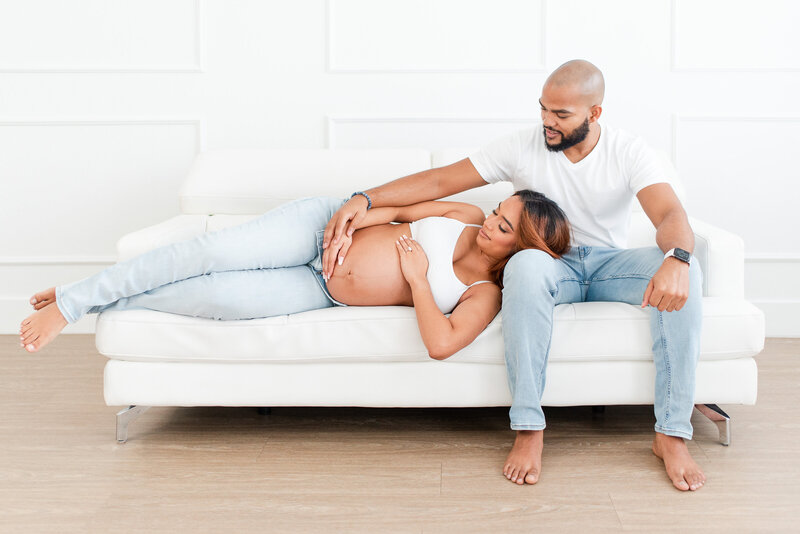 maternity session new mom and dad on couch in miami all white studio by miami maternity photographer msp photography David and Meivys Suarez