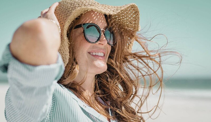 Midlife woman , sunglasses, straw hat, at the beach
