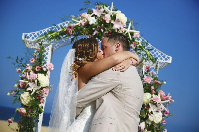 Jersey Shore Wedding | Couple Kissing on Beach After Ceremony with Arch and Blue Sky on a Summer Afternoon | New Jersey