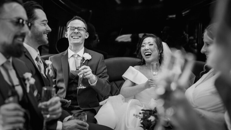 Bride and groom belly laughing with friends in a limo on their wedding day, a candid and joyful moment captured in PJ style.