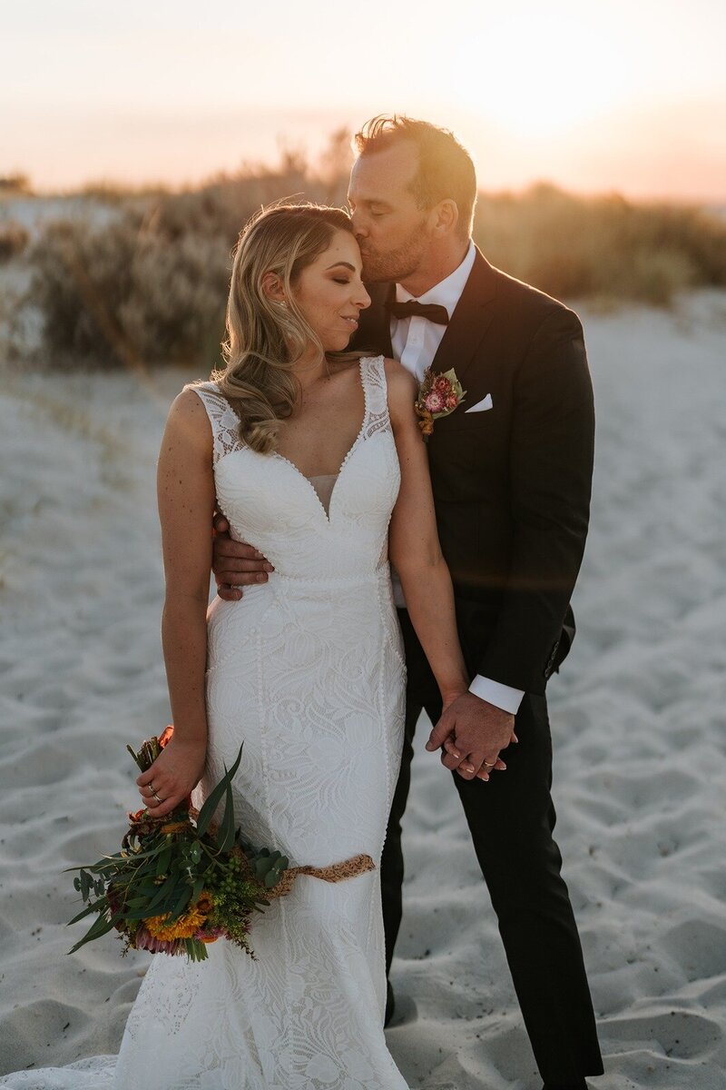 A bride and groom on the beach at sunset