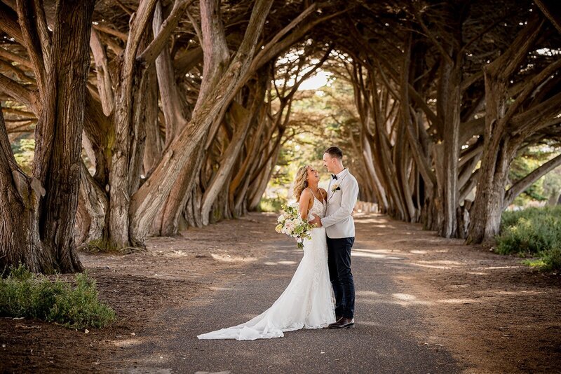 A bride and groom standing in front of a large bush for wedding photos