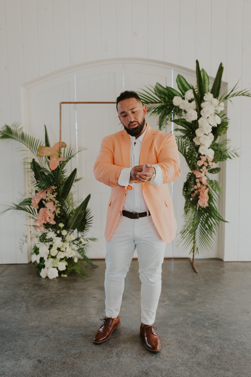 Groom getting ready for his wedding day in front of tropical summer floral archway