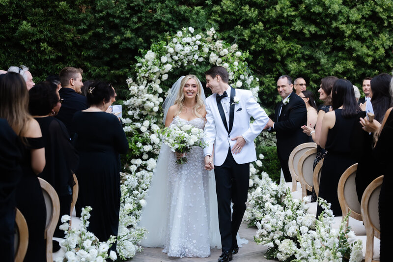 Wedding Photographer, bride in her dress and groom in his tux walk hand-in-hand down the beach