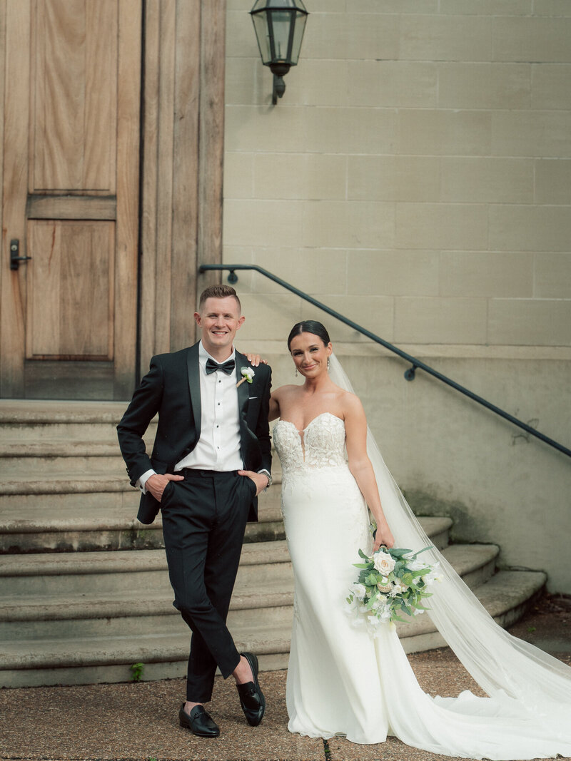 Bride and groom posing on stone steps outside historic building with soft overcast lighting