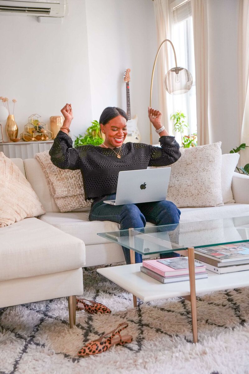 jacinta-gandy-smiling-and-raising-hands-while-working-on-laptop-in-modern-living-room-03