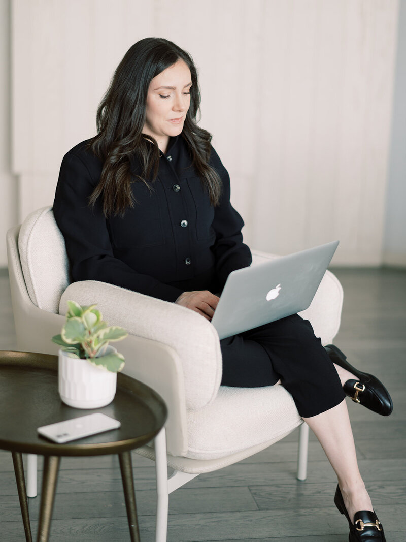 Carina, from Corporate Events Hamilton wearing a white pinstripe button up shirt working on her laptop around some flowers at the Pearle Hotel