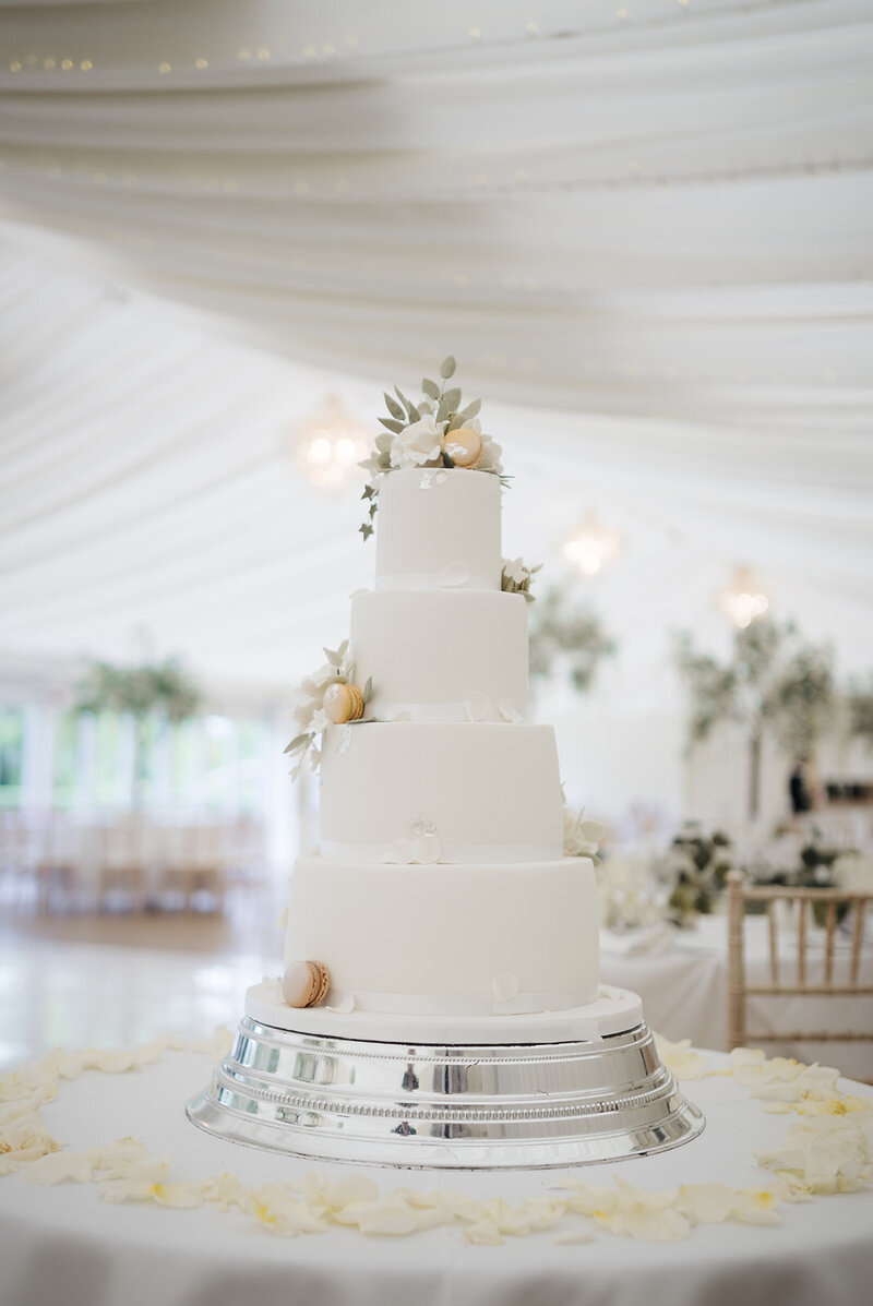 A white/cream wedding cake with gold details and pastel flowers.