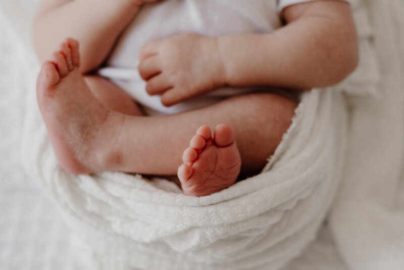 Detailed newborn photo of baby's feet with white blanket.