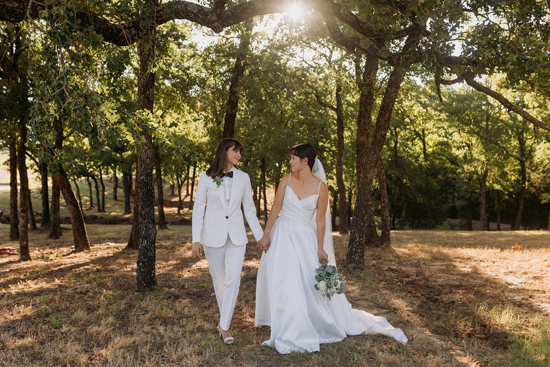 Brides walk through trees while holding hands