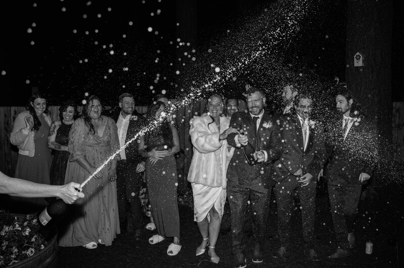 Black and white photo of a wedding party celebrating together with a champagne spray during Portland, Oregon wedding reception. 