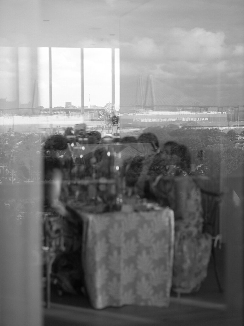 Wedding guests enjoy their wedding reception, with Charleston skyline reflected through a window