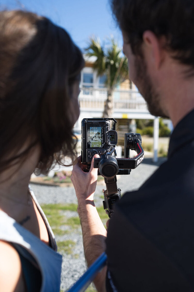 a closeup of a camera screen,  shot is framed by a man and a woman in a coastal area