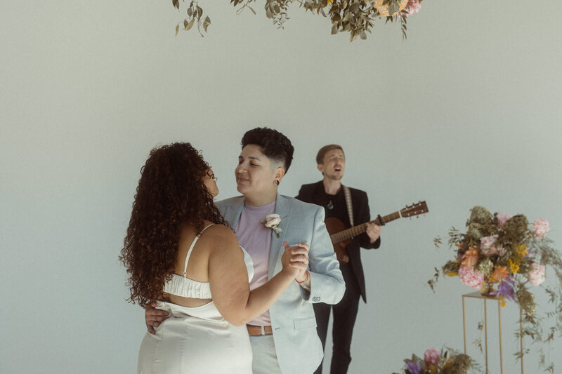 A wedding couple during their first dance with a person singing and playing guitar behind them.