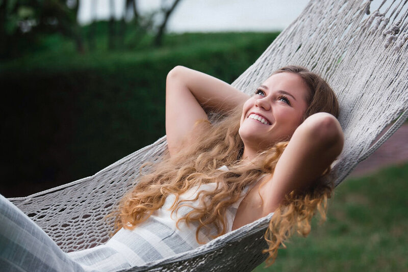 Senior girl lays back in hammock with arms crossed behind her head smiling to the sky