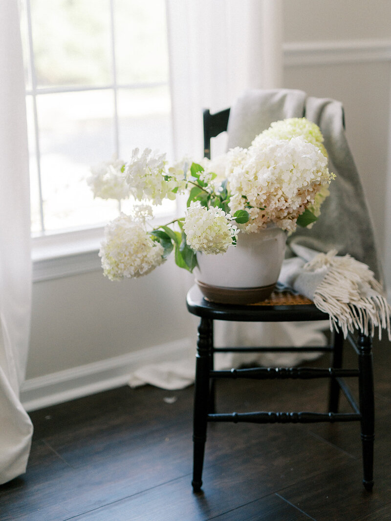 White hydrangea arrangement in ceramic pot on rattan chair with blanket throw