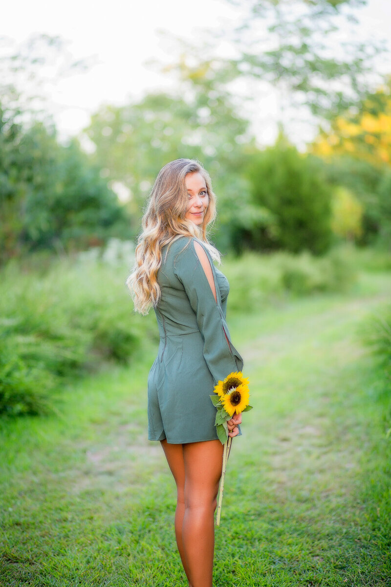 Female holding sunflowers in green jumper in the grass