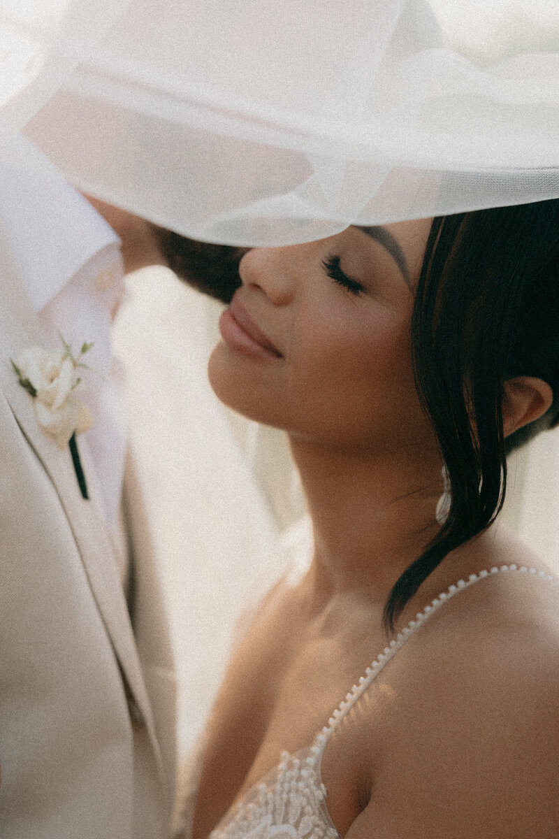 Close up portrait of groom kissing bride on the cheek underneath her veil