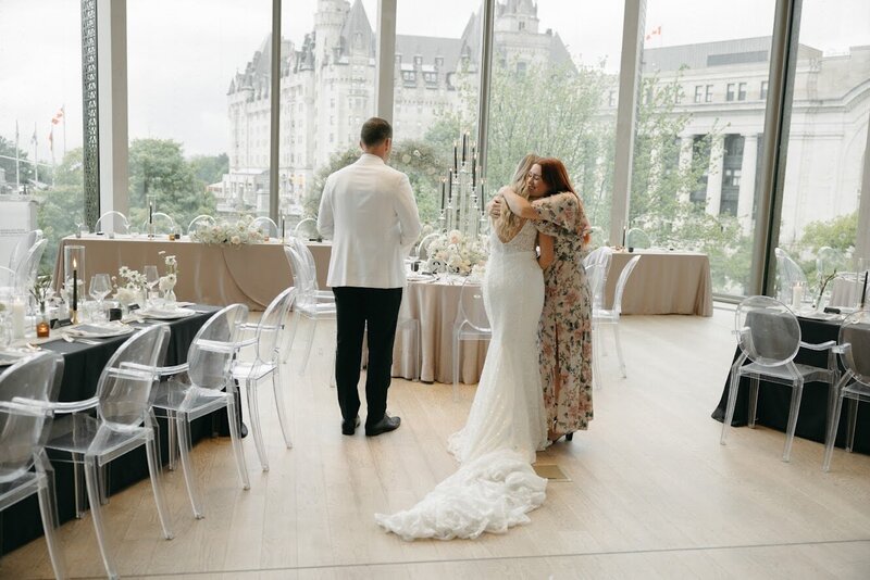 A heartwarming image shows a couple joyfully embracing designer Brittany Frid, celebrating their stunning wedding decor at the National Arts Centre's O'Born Room.