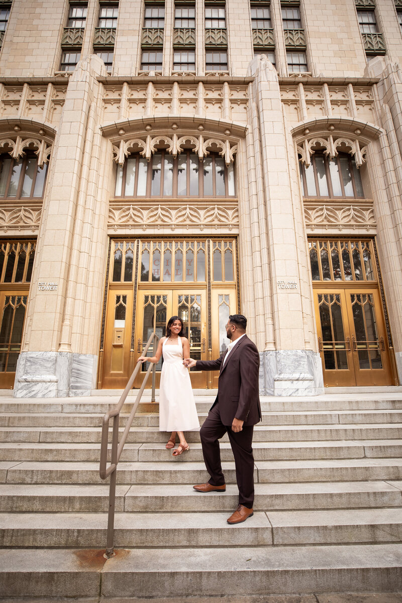 engaged couple shares a kiss on the grand stone steps of atlanta city hall, standing in front of ornate gold doors during a romantic downtown engagement photo session