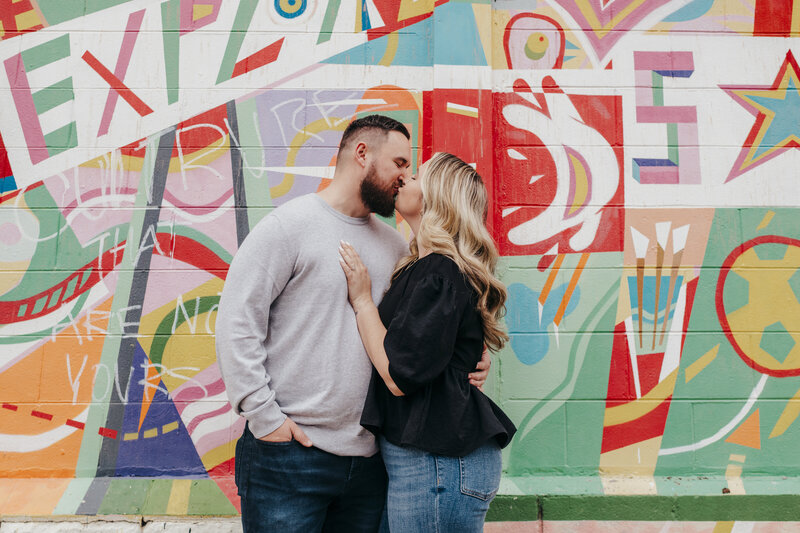 couple kissing by colorful mural in savannah engagement session