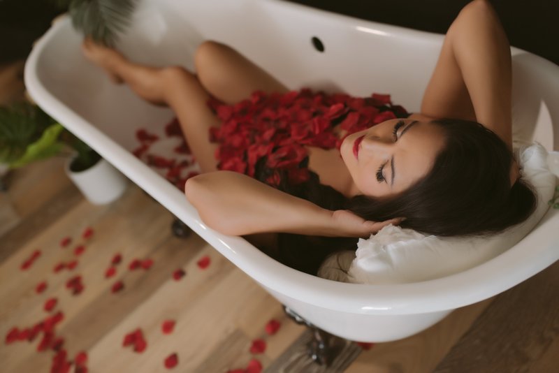 Woman lying in a bath tub covered by rose petals for boudoir photoshoot
