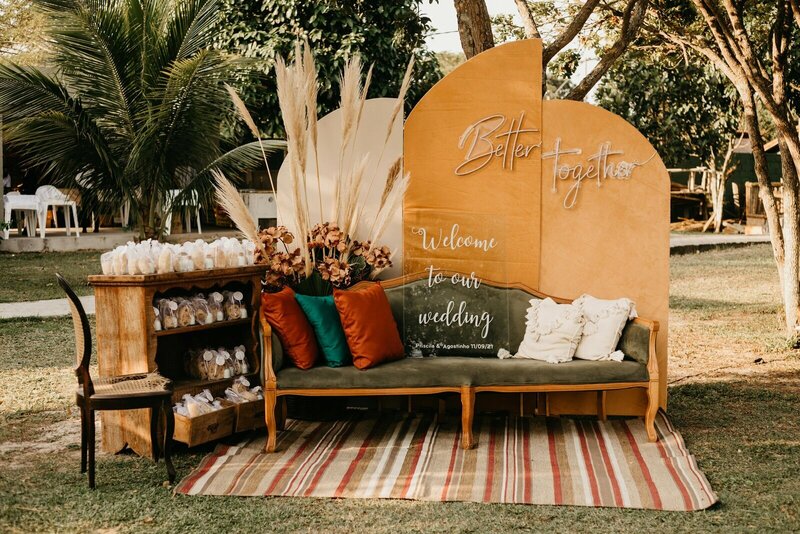 Décor de photobooth imaginé par une décoratrice de mariage. Canapé en velours coloré entouré de meubles vintage et de pampas.