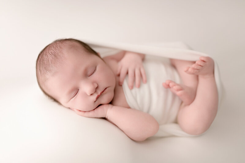 Fine-art newborn image of baby girl in Huck Finn pose, styled in all white and photographed in Paris, Ontario.