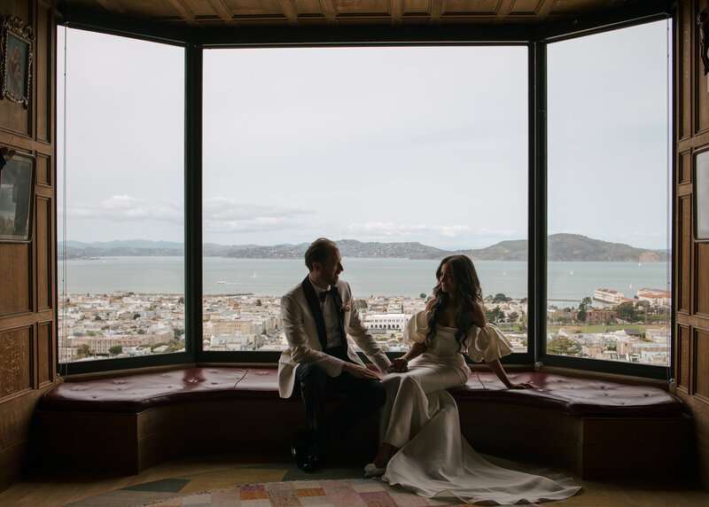 Bride and groom share a moment looking at each other at Flood Mansion in San Francisco surrounded by lush deep red color floral arrangements. 