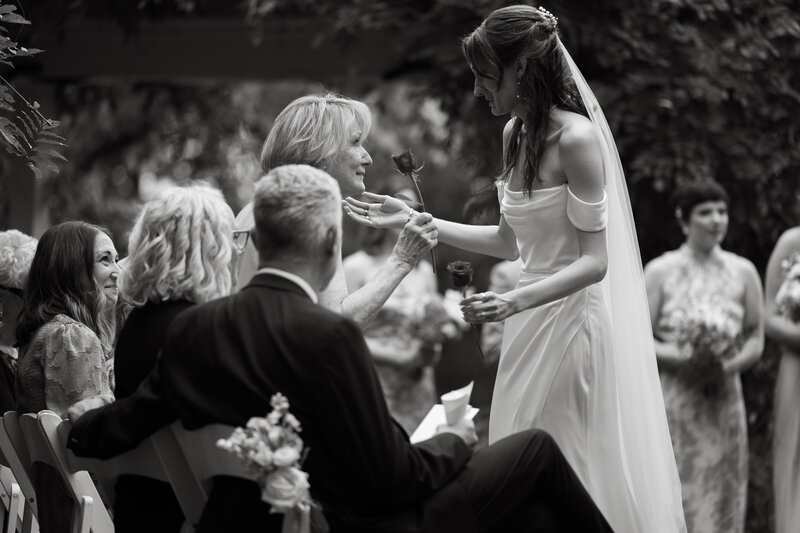black and white photo of bride giving grandmother rose during wedding ceremony