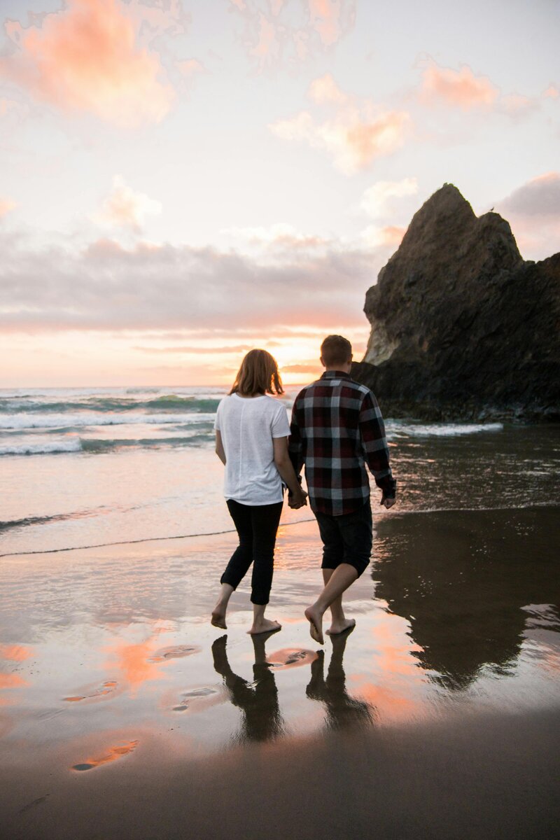 A man and woman holding hands walking on a beach