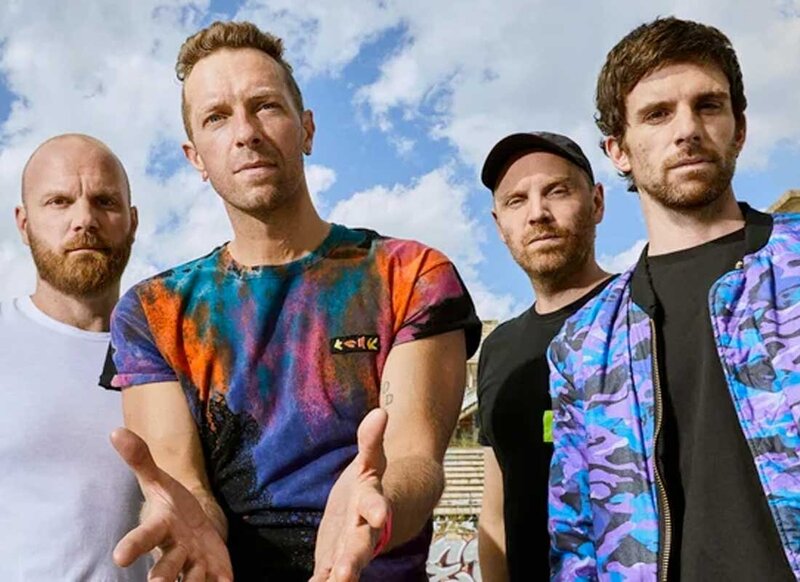 Coldplay band posing staring at camera against a blue sky background