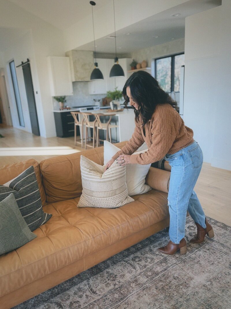 interior designer is fluffing pillows after designing a boho living room