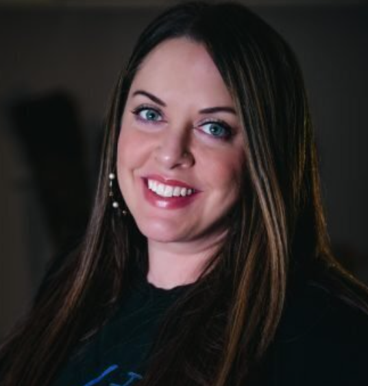 Amanda smiling, sitting in a chair at vIVid wearing black scrubs