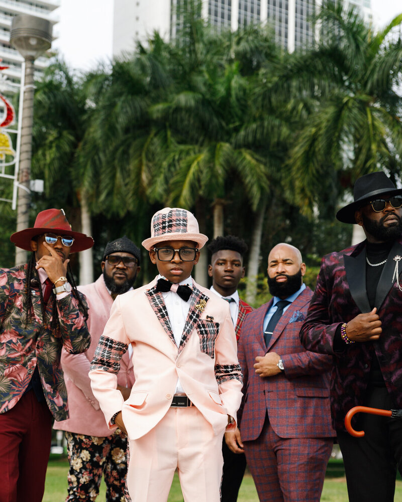 A group of black men in suits surrounding a young black boy wearing a suit in downtown Miami.