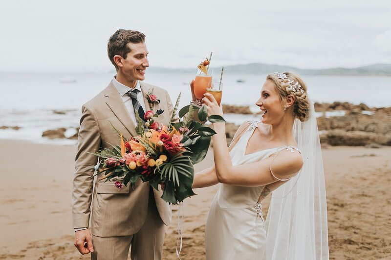 A Colorado wedding photography bride and groom clinking their drinks with water and mountains behind them