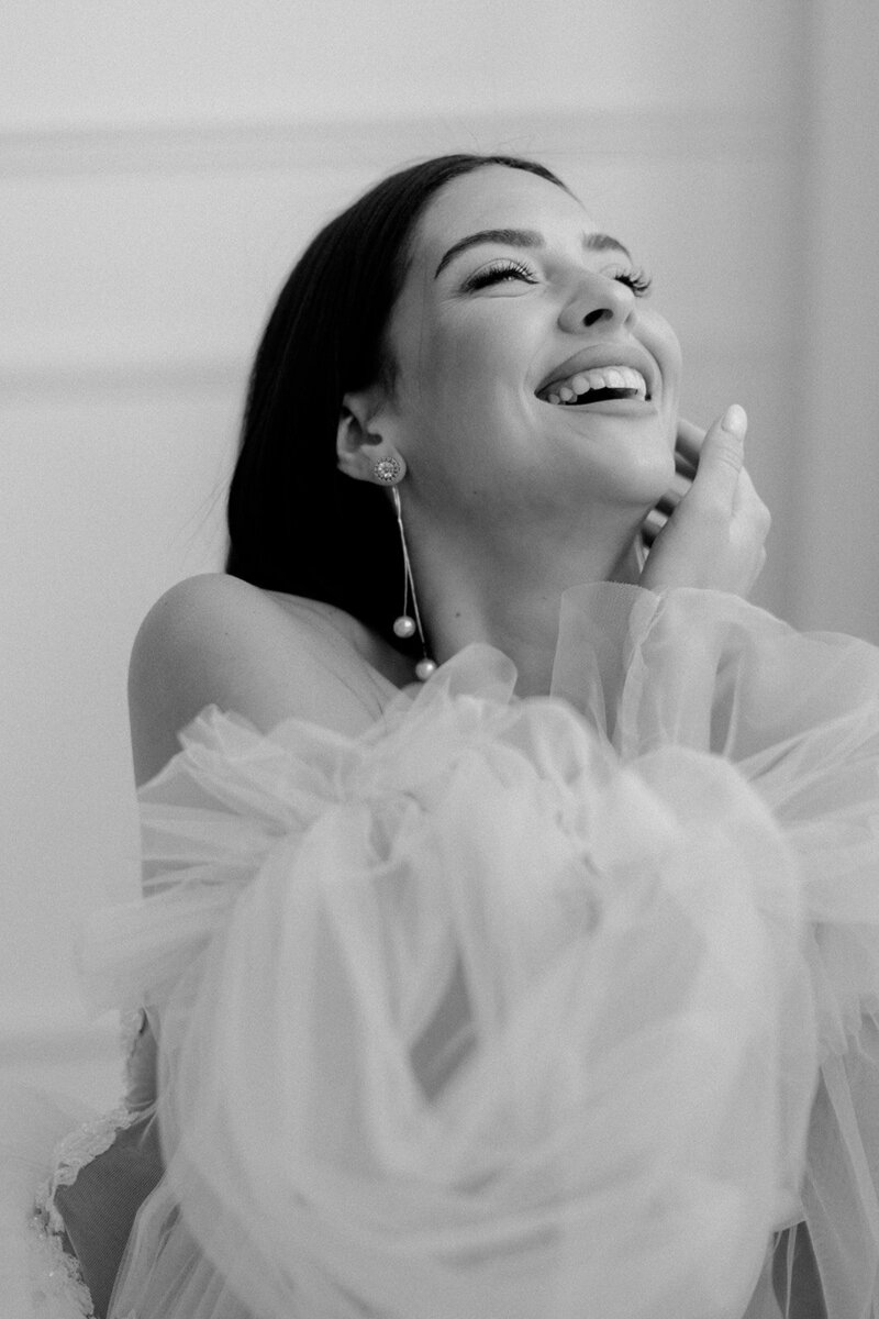 A laughing bride in a ruffled dress, enjoying a candid moment in black and white.