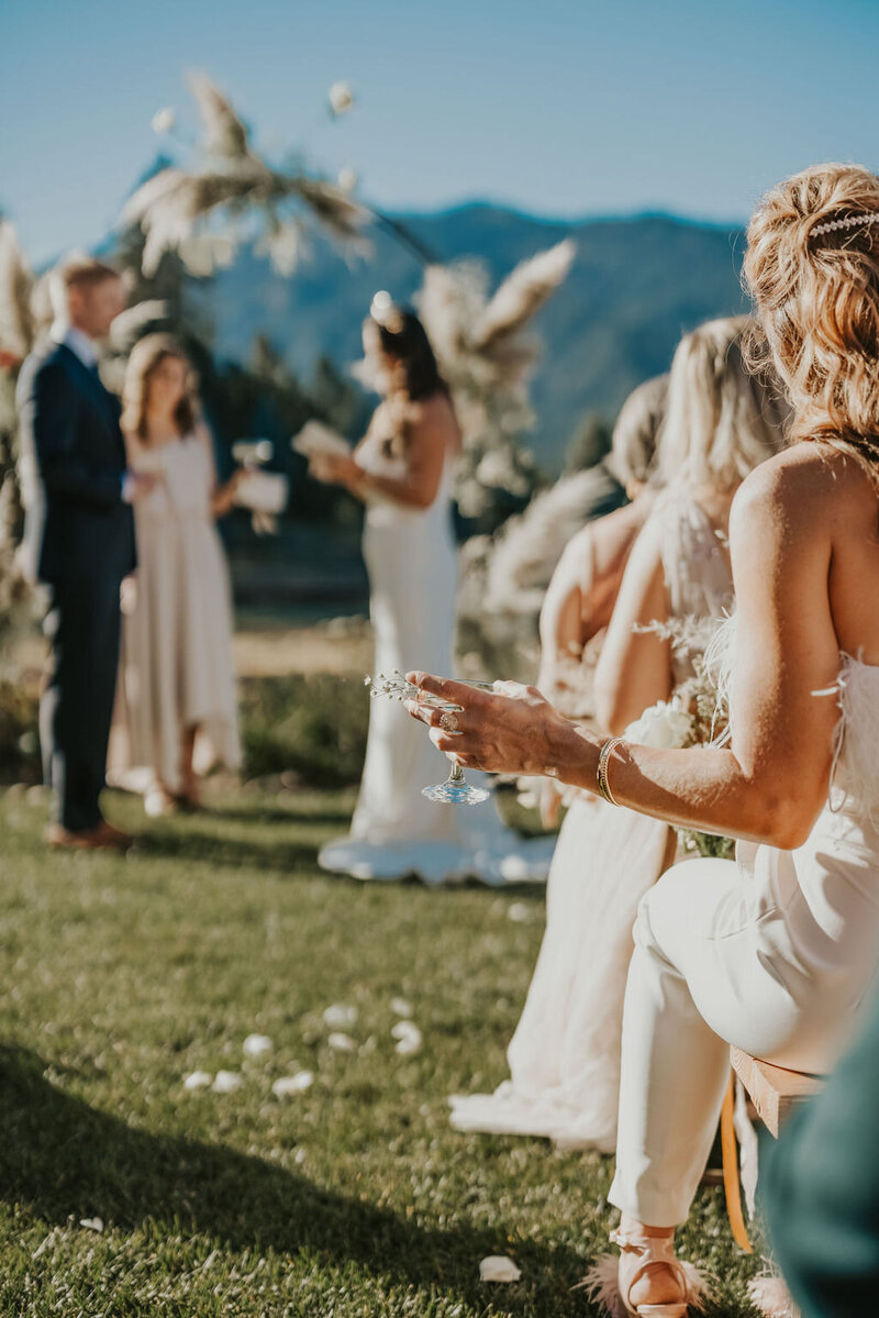 A guest holds a cocktail in hand while seated at an outdoor wedding reception, representing wedding coordination services offered by Perfect Thirds & Co.