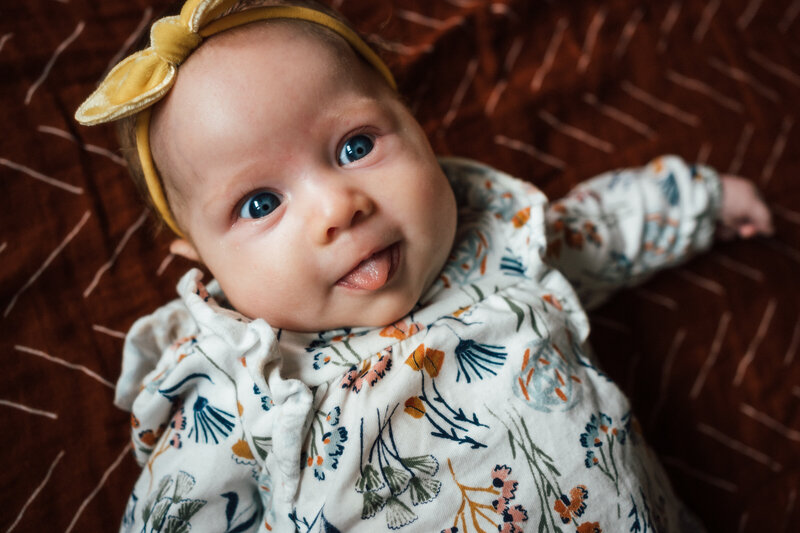 Baby wearing yellow bow sticking tongue out