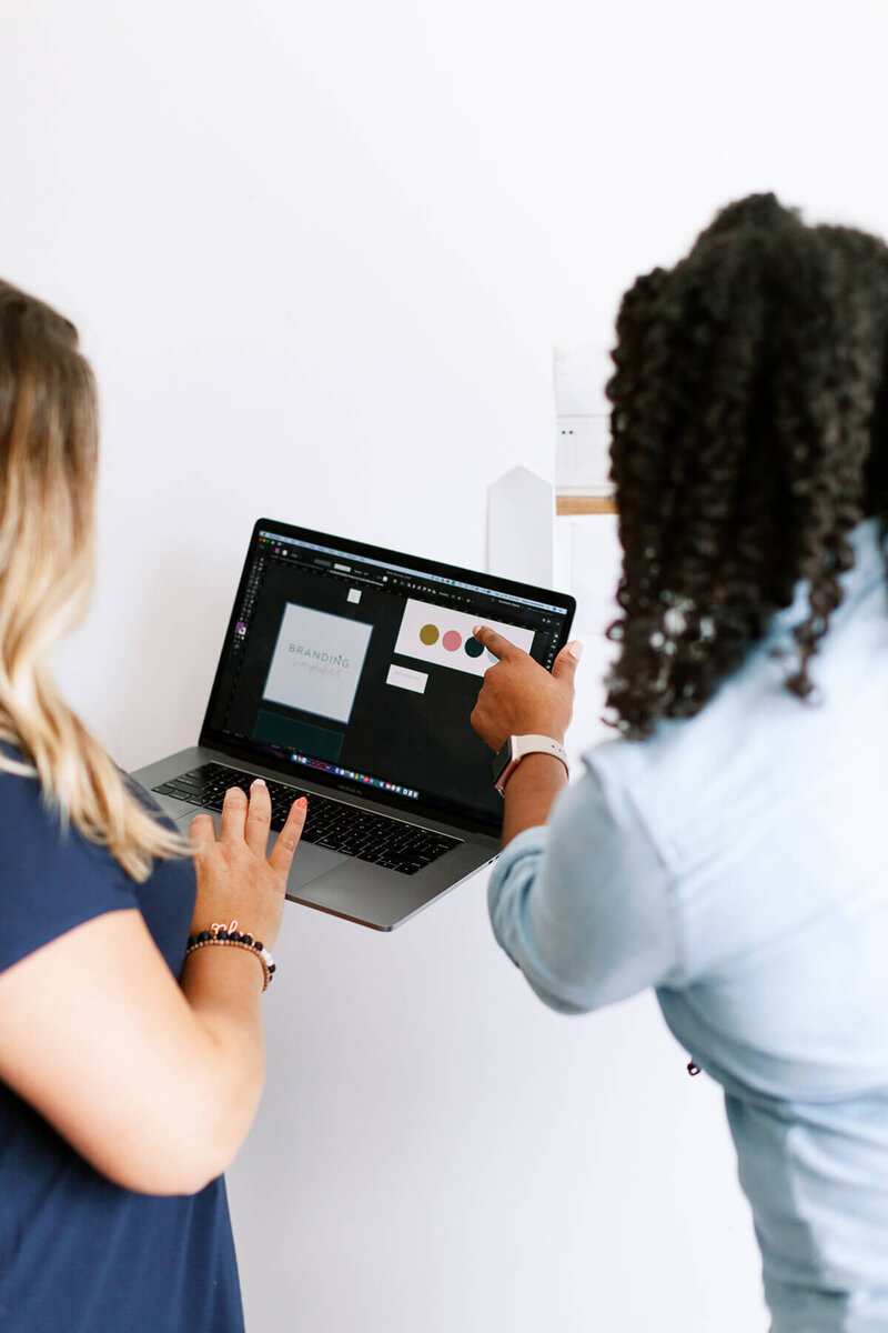 woman pointing to a color sample on a computer screen another woman is holding