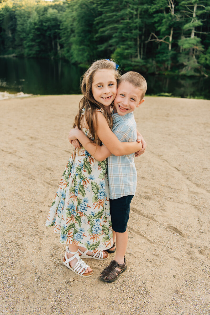 Brother and sister hugging in front of lake