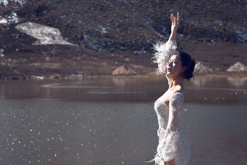 DraDramatic shoot of a bride in a haute couture dress by an alpine lake in snow capped mountains.matic shoot of a bride in a haute couture dress by an alpine lake in snow capped mountains.