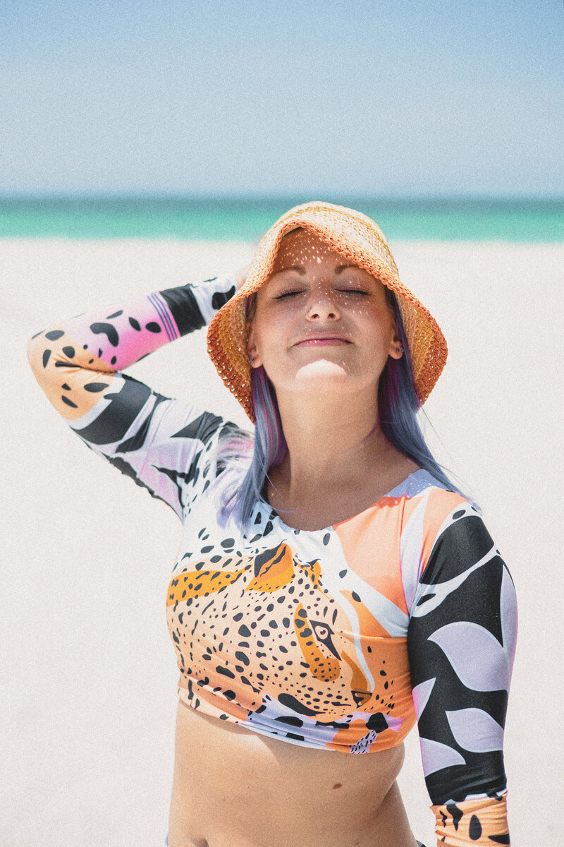 Model wearing woven bucket hat and long sleeve rash guard while standing on beach in Florida