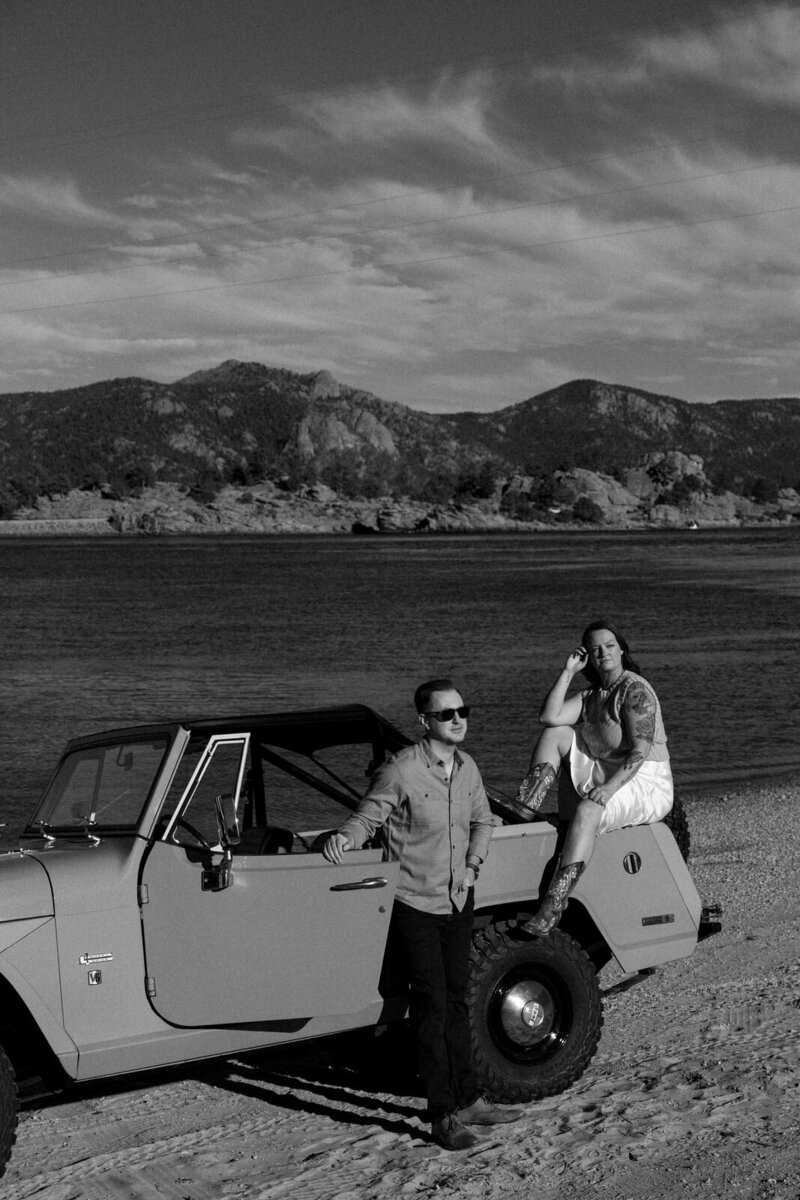 Man and woman sitting on a jeep during their engagement session in the Rocky Mountains in Colorado with a lake behind them, by Andrea-Marie Photography